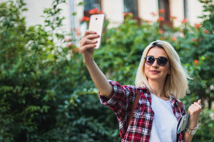 A woman wearing sunglasses taking a selfie photo outdoors in good lighting