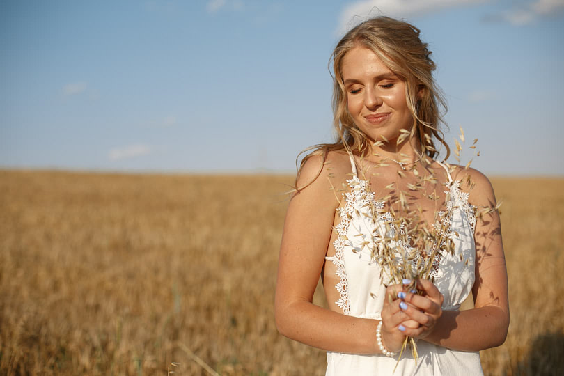 A woman with boho bridal makeup on standing in the middle of a field with flowers in her hands