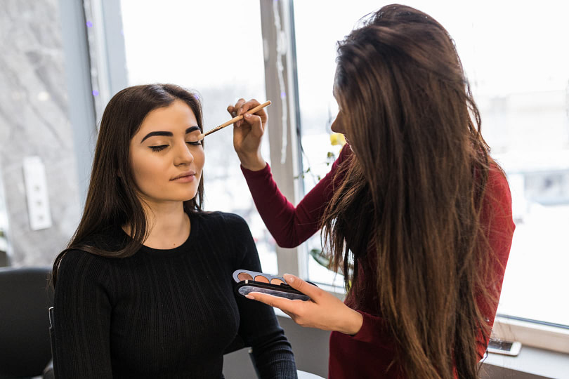 A makeup artist applying eyeshadow to a woman sitting in a chair