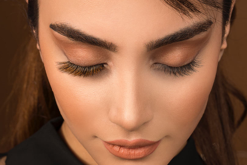 Close-up of woman wearing tan eyeshadow and false lashes with her eyes closed