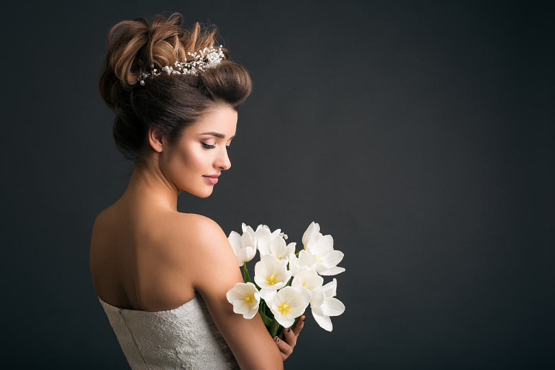Woman wearing wedding dress holding flowers while looking over her shoulder