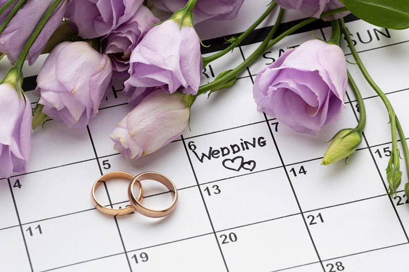 Calendar with wedding written on it with purple roses and wedding rings on top