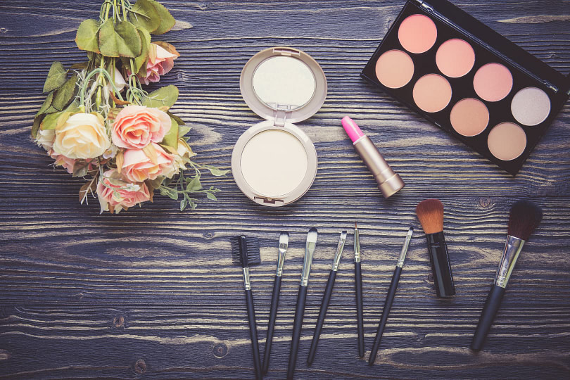 Top-down view of a wooden table with a flower bouquet and various makeup products