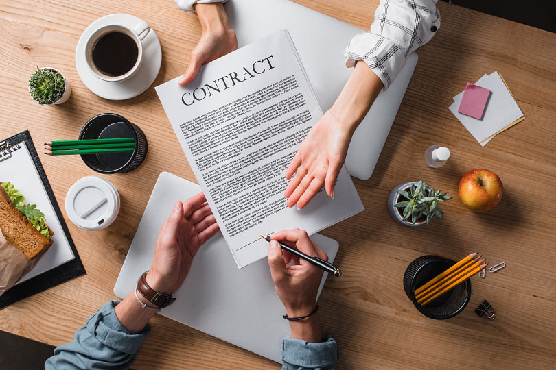 Contract being passed over a table between a vendor and client for review