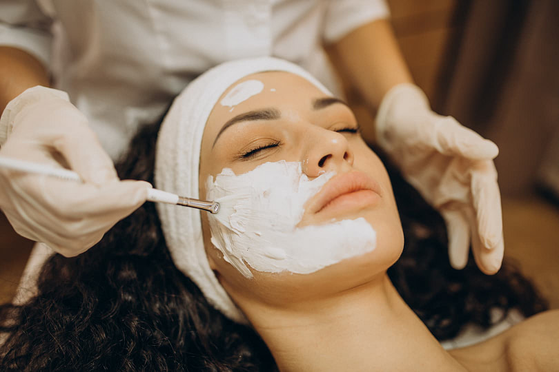 A woman lying down getting a skincare treatment done on her face by a professional