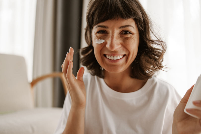 A woman putting sunscreen on her face while smiling