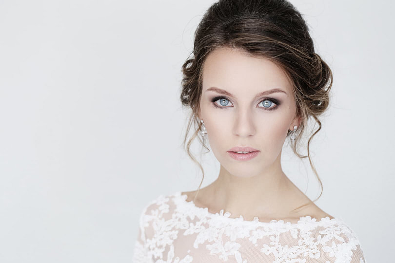 Woman with classic bridal makeup on wearing a wedding dress in front of a grey background