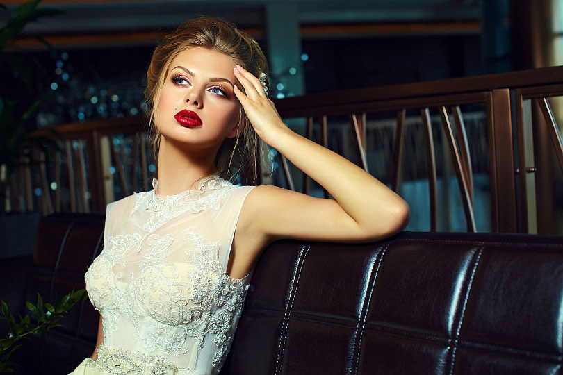 Woman with glamorous bridal makeup on sitting on a row oh seats with a wedding dress on
